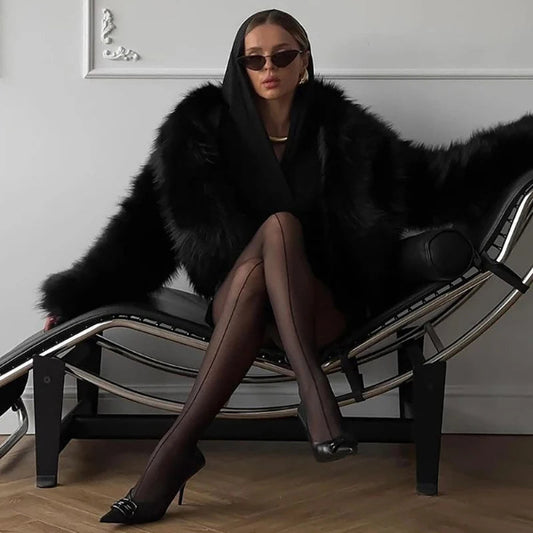 Modell trägt transparente Damenstrumpfhose 20 DEN mit schwarzem Mantel und Sonnenbrille, stilvoll in einem modernen Raum.
